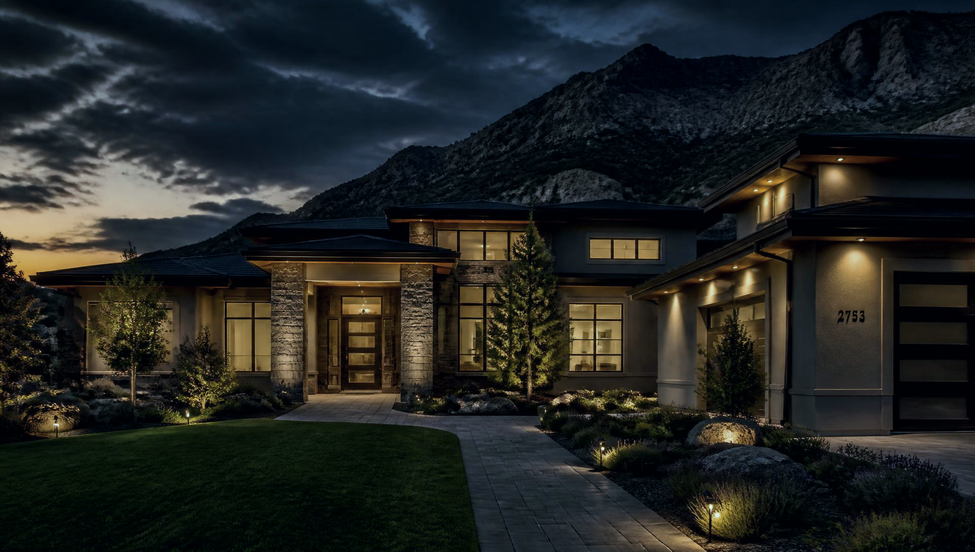 Modern Utah home at dusk with landscaped yard and warm exterior lighting